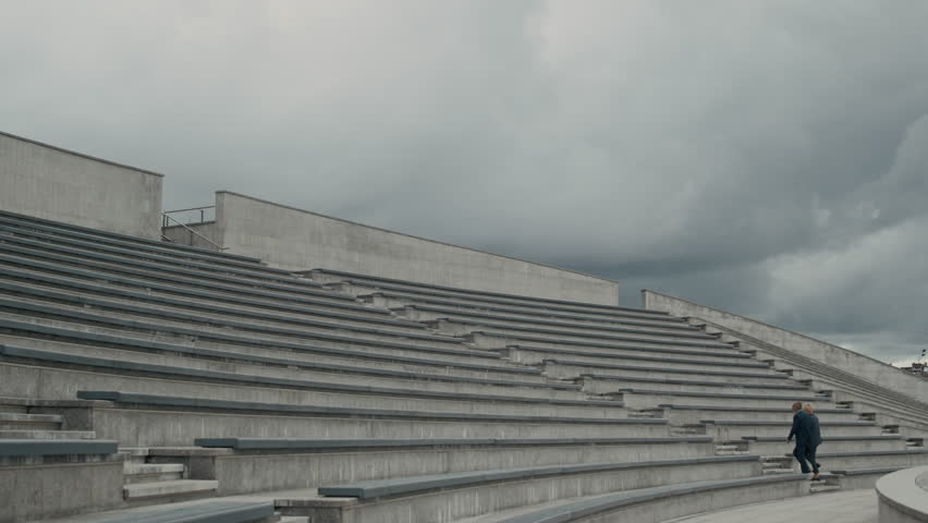 Wide shot of two entrepreneurs walking upstairs on contemporary city tiered staircase on cloudy day