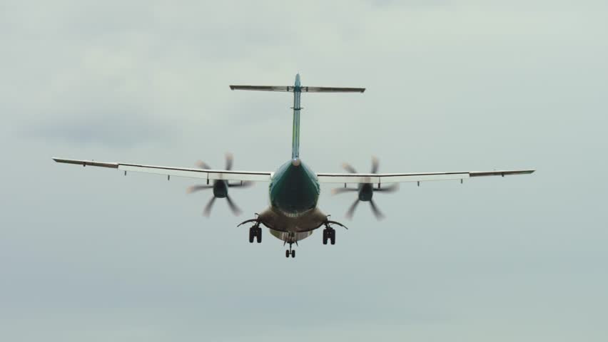 Turboprop passenger plane landing on wet runway in overcast weather with low visibility and strong crosswinds. Aircraft touching down in rainy conditions during unstable approach. Propeller plane
