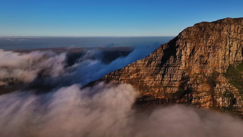 Aerial view of the iconic Table Mountain partially veiled by ethereal clouds, a dance of light and shadow across its rugged face, Cape Town, Western Cape, South Africa.