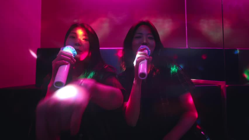 Two Korean girl friends singing K-pop song in a noraebang karaoke, having fun together on saturday night