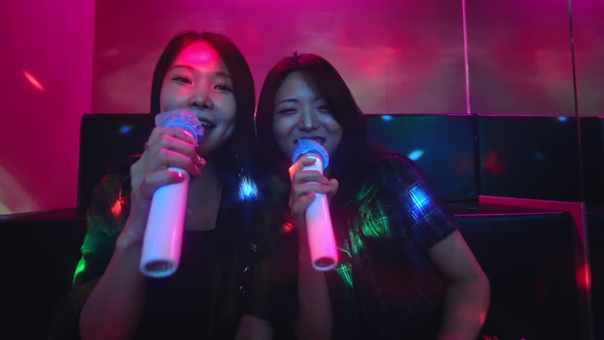 Two Korean girl friends singing K-pop song in a noraebang karaoke, having fun together on saturday night