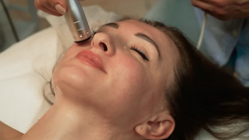 Female undergoing expert facial massage in luxury aesthetic clinic. Ultrasound Fat Reduction, High-Frequency Facial Therapy. Skin improvement, facial firming, age-correcting method for older client