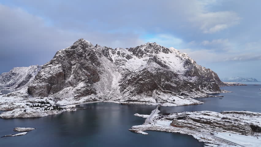 Cinematic aerial view of Henningsvær, a charming fishing village in Lofoten, Norway, surrounded by snowy mountains, Arctic waters, colorful houses, and iconic coastal scenery in winter