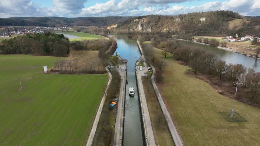 An aerial view of a boat in the middle of a lock system on the Danube Canal in Germany. Highlights the engineering of the waterway and the surrounding natural landscape.