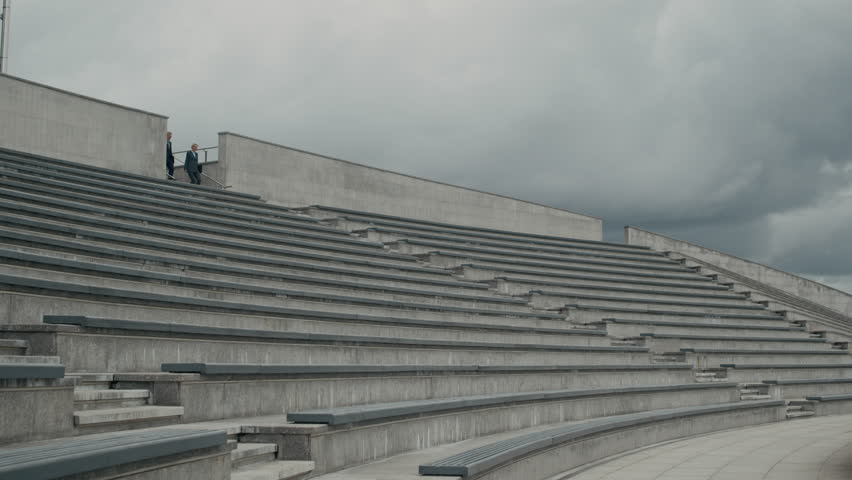 Wide copy space shot of two adult business colleagues in suits going downstairs on contemporary tiered city staircase