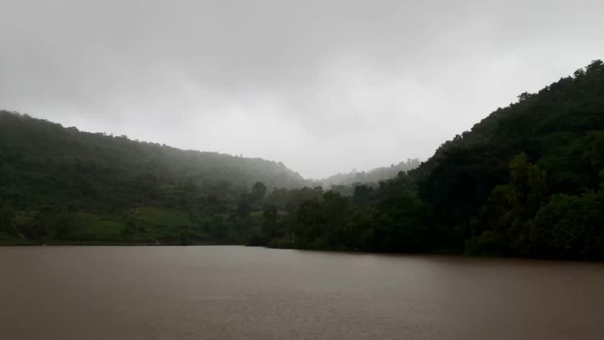 mountain pond surrounded by dense forest, with heavy rain pouring over the wild, scenic landscape.
