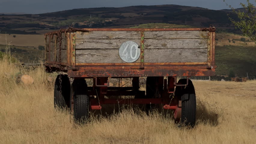 A lone vintage tractor trailer sits on a remote hill amid a sparsely cultivated landscape.