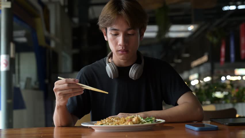 Pad Thai noodles eaten with chopsticks in Thailand by young tourist man during day. Famous street food cuisine loved by tourist and locals in Asia.