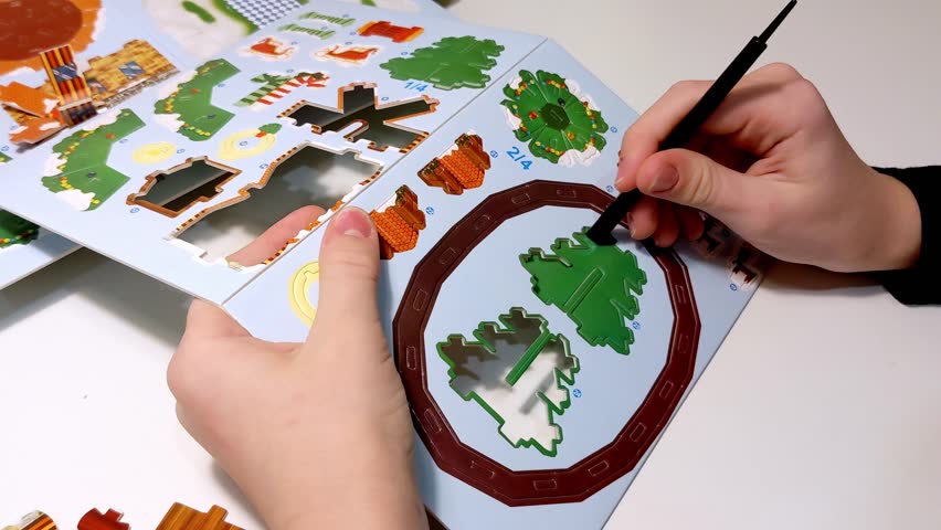 A child uses a tool to push out a brown piece from a Christmas craft kit. A step by step process