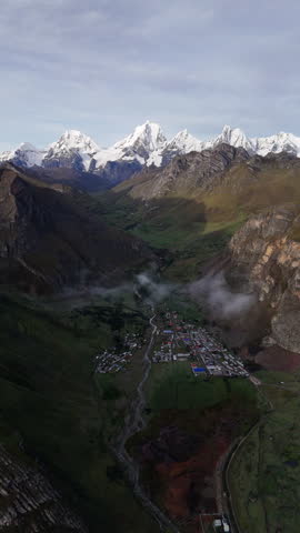 Cinematic aerial view of dramatic mountain valley at sunrise in Peru, glowing sky with clouds and rugged peaks, serene landscape with winding river and travel destination mood - Vertical format
