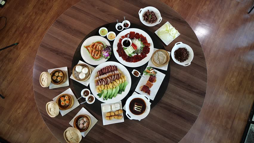 A luxurious Chinese banquet spread displayed on a round dining table, featuring Peking duck, dim sum, roasted meats, and assorted side dishes for a festive family meal.
