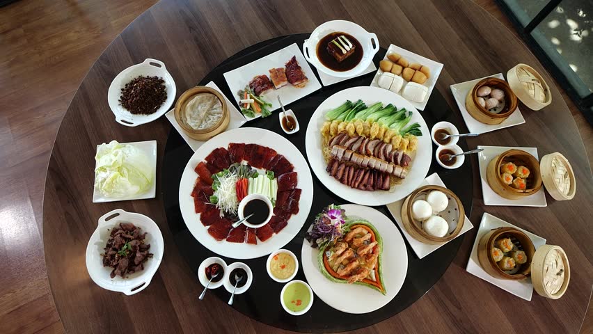 A luxurious Chinese banquet spread displayed on a round dining table, featuring Peking duck, dim sum, roasted meats, and assorted side dishes for a festive family meal.