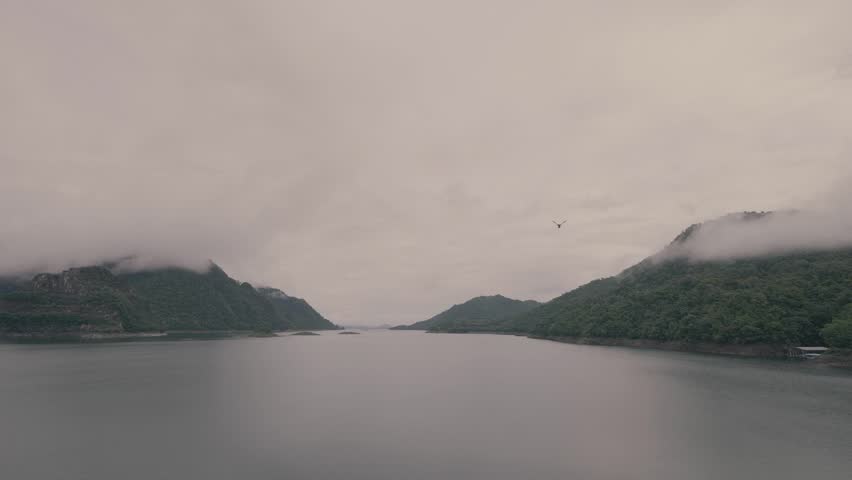 Tranquil lake view surrounded by misty mountains, with a small green island in the middle of calm waters.
