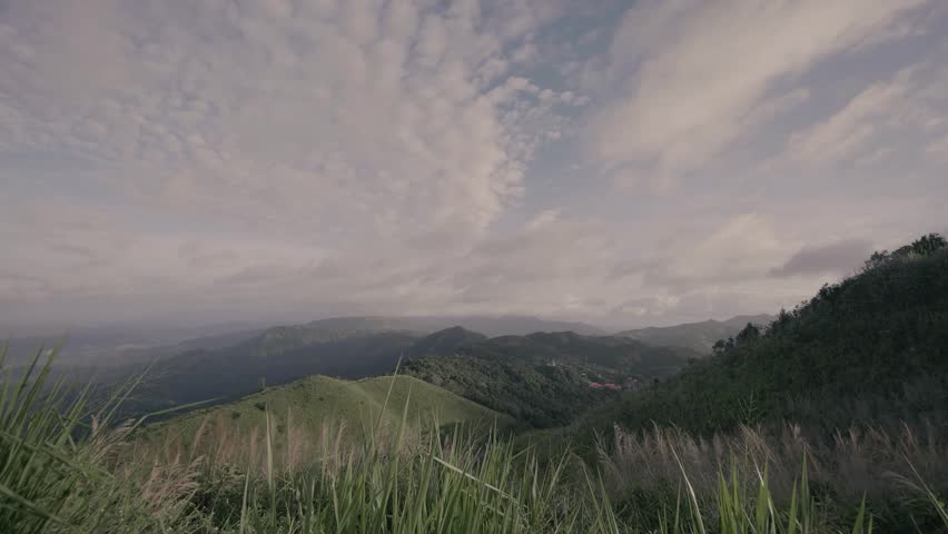 Scenic view of green mountain hills under a cloudy sky, with tall grass in the foreground creating a peaceful natural landscape.