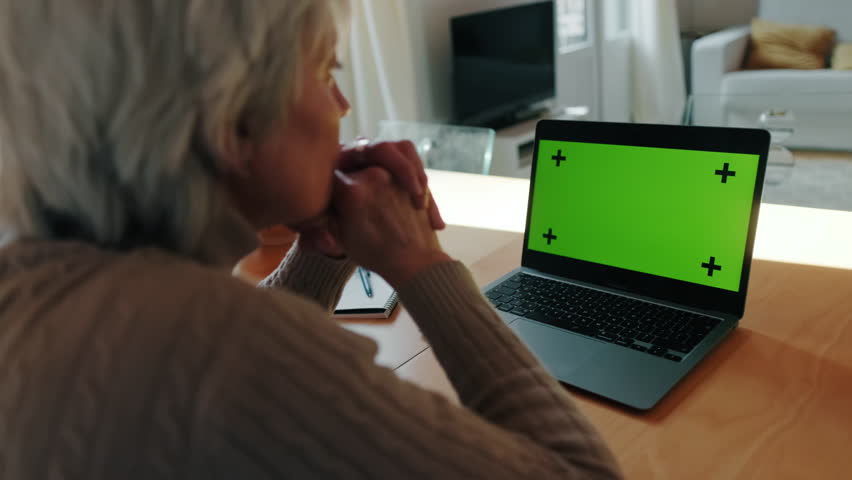 Senior woman concentrating on a laptop with green screen. Perfect for mockups and presentations.