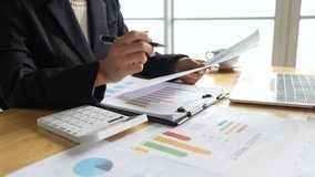 A businessman calculates finances using a calculator, analyzing charts and graphs on documents, while working with laptop and smartphone in office. - Powered by Shutterstock - Get 15% off with code: PIKWIZARD15