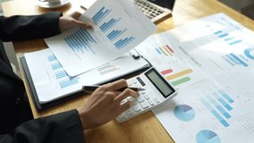 A businessman calculates finances using a calculator, analyzing charts and graphs on documents, while working with laptop and smartphone in office. - Powered by Shutterstock - Get 15% off with code: PIKWIZARD15