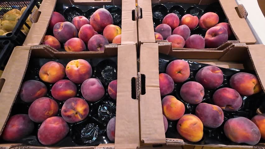 Kiwi and nectarine fruits in plastic crates and cardboard boxes in a supermarket.