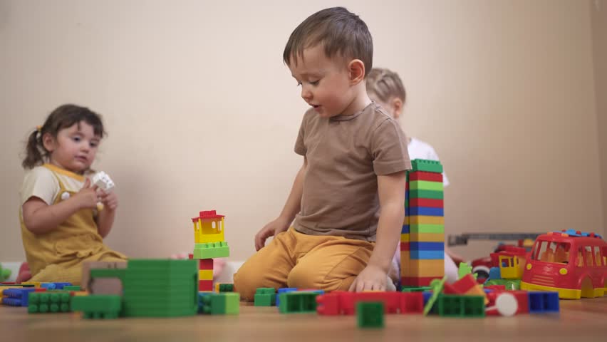 Three children playing with blocks. Children play together in a group. Build a new floor for your kindergarten with toys lifestyle and a constructor. Three kids engaging with building blocks.