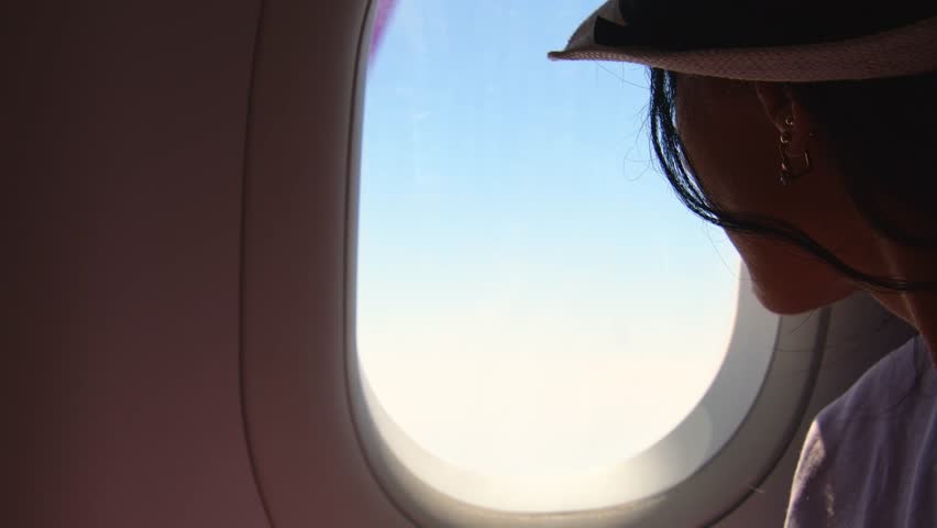 Caucasian Woman looks out the window of an flying airplane. Young caucasian happy passengers are traveling by plane, watching the sky from above and hold passport