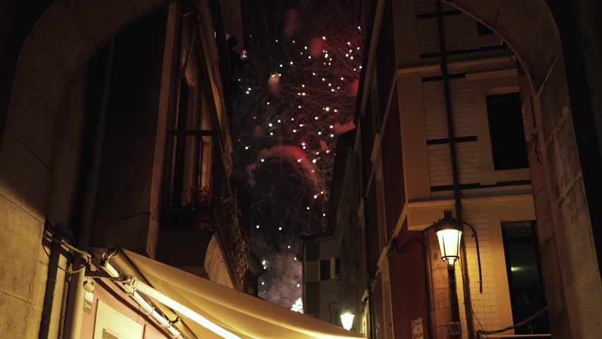Cinematic view of fireworks bursting between old European streets at night, celebration, holiday, festival, magic, tradition, architecture, history, culture, New Year, color, atmosphere, joy, fiesta