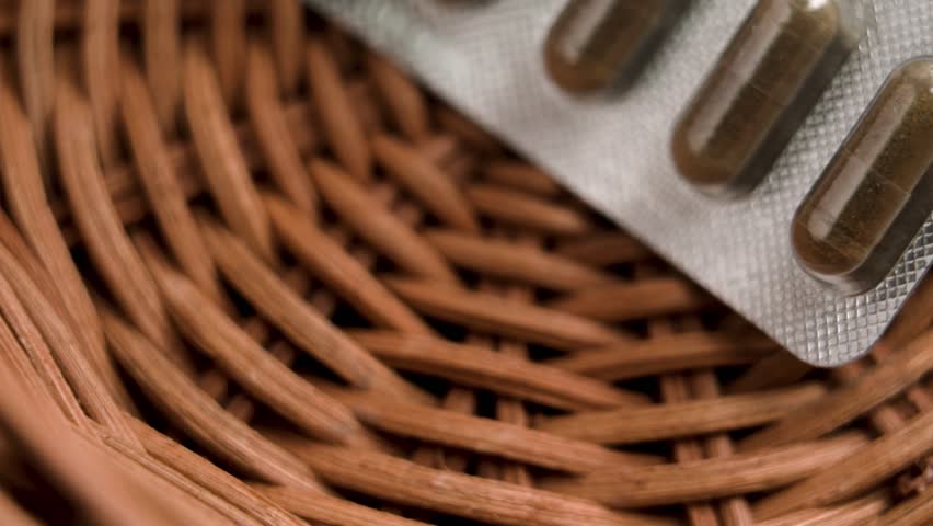 Foil blister pack of pharmaceutical natural herbal capsules falling into eco-friendly wooden bowl