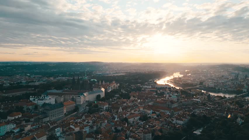 Experience the breathtaking view of Prague Castle as the sun rises over the city. The golden light illuminates the Lesser Town and the historic structures below, creating a serene atmosphere.