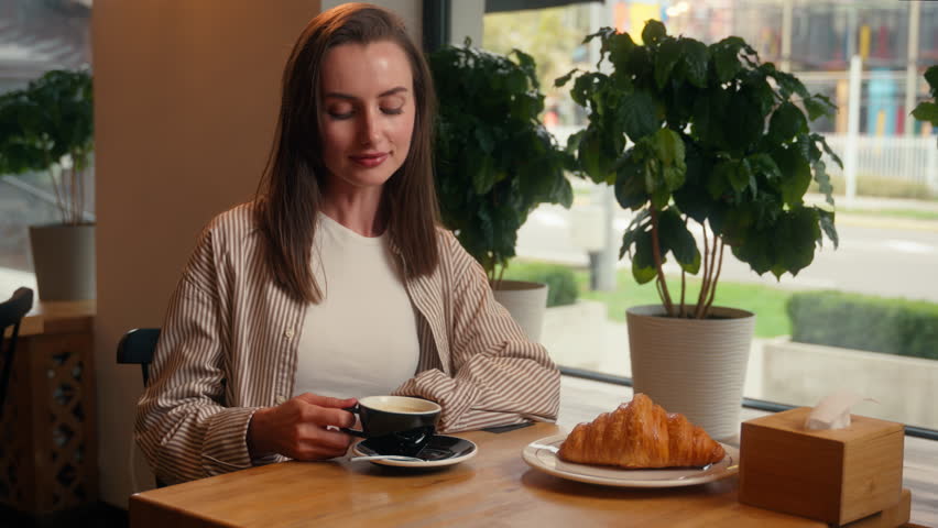 Caucasian woman drinking tasty good coffee in cafe girl female cafeteria visitor drink tea showing thumb up like gesture recommend restaurant food nutrition with croissant at table smiling at camera