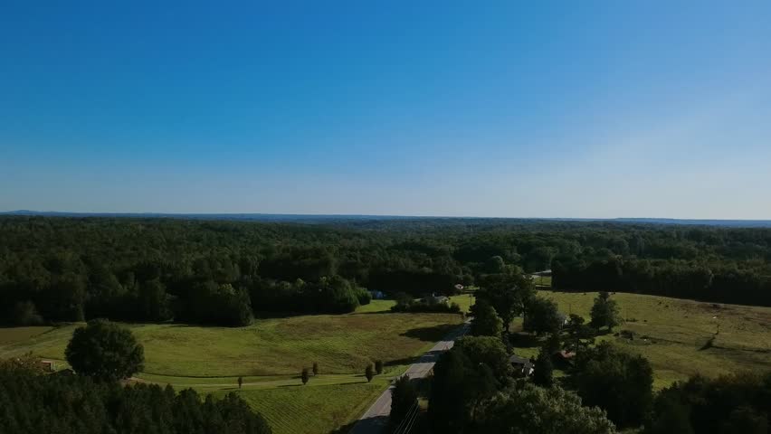 Drone descending over a rural road in North Carolina, aerial view of countryside fields and farmland with scenic rustic landscape and trees