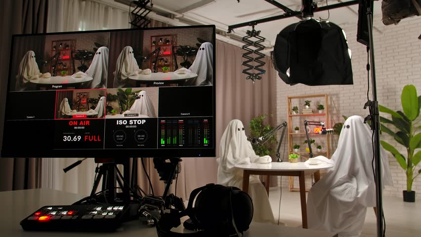 Backstage in the studio, a two people dressed as ghosts, wearing white sheets, record a podcast at a studio table with microphones. Perfect for Halloween, comedy, and entertainment.