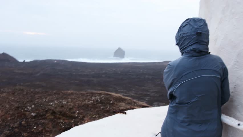 Woman tourist stand by building hold on hardly can stand in extreme Icelandic weather in south coast by atlantic ocean. Travel Iceland changeable weather and high winds forecasts