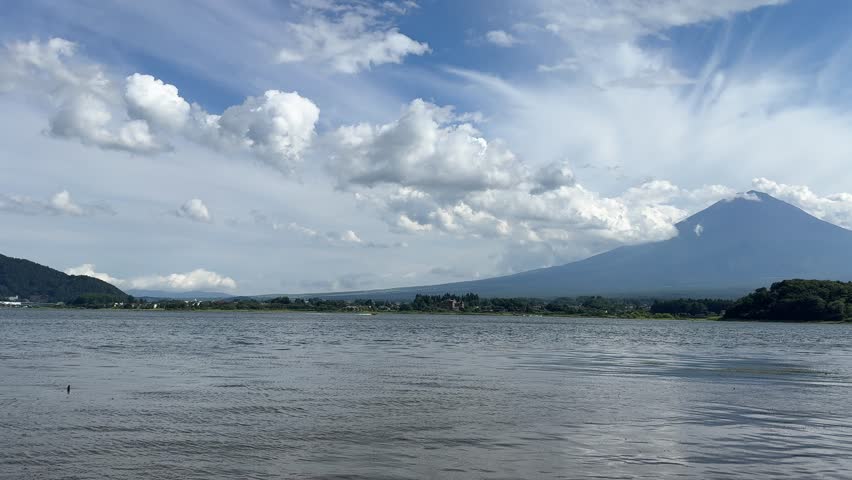 Scenic landscape of Mount Fuji with lake water and dramatic clouds in the sky, Japan. Iconic Japanese mountain view, perfect for travel, tourism, meditation, nature, and cultural projects.