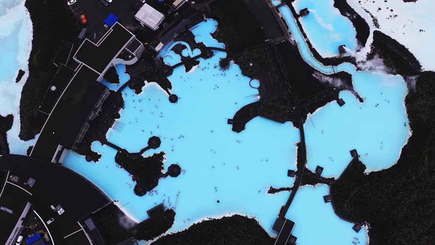 Aerial view of the Blue Lagoon Spa in Iceland, with bright blue geothermal waters, black lava fields, rising steam, and integrated walkways.