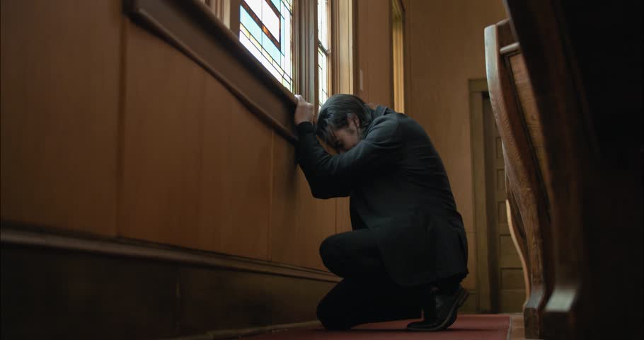 A Christian man praying and kneeling inside old church building.