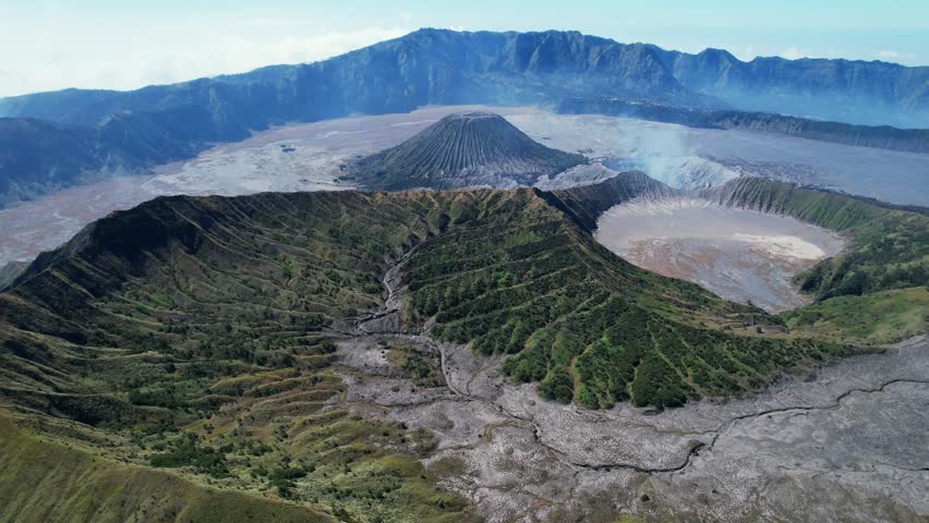 Drone reveal of Mount Bromo smoking in East Java, showing the vast Tengger caldera with Mount Batok in the distance. Unique aerial view from the north side of this iconic volcano