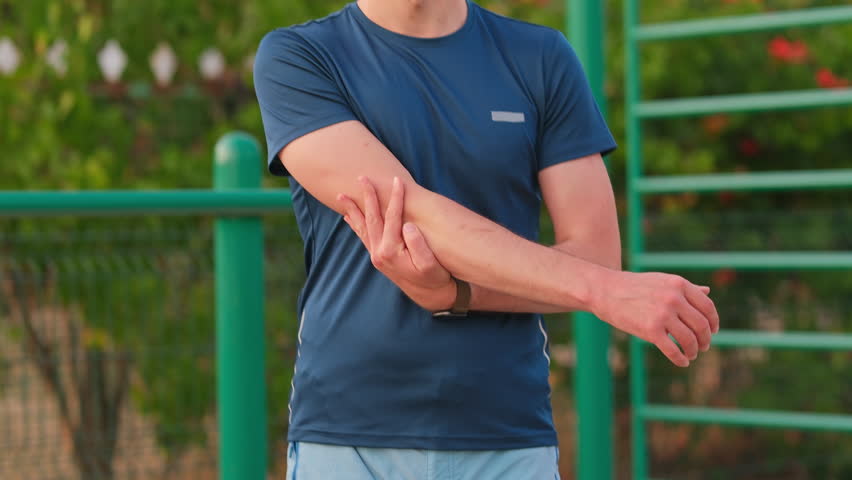 Close up shot of a man stretching his elbow after a workout. Outdoor summer exercise