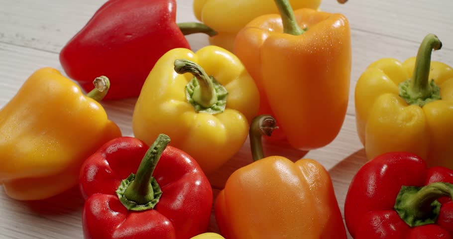 A close-up shot of various bell peppers in red, yellow, and orange on a light wooden surface. The peppers are fresh and vibrant, perfect for healthy cooking. Vibrant Fresh Vegetables