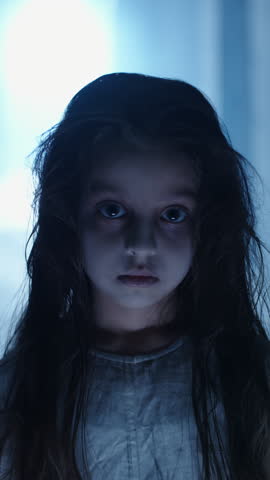 Scary little girl in horror style dirty dress messy hair spooky eyes dark circles angry look Halloween cosplay creepy child character haunted corridor dim flickering ceiling light frightening scene