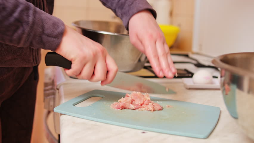 Close up shot of a woman mincing chicken breast manually with a knife.