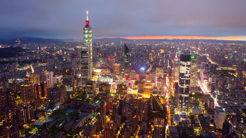 Aerial hyperlapse above XinYi District in Downtown Taipei, vibrant capital of Taiwan, where 101 Tower stands out amid modern skyscrapers and city lights dazzle in twilight under dramatic sunset sky