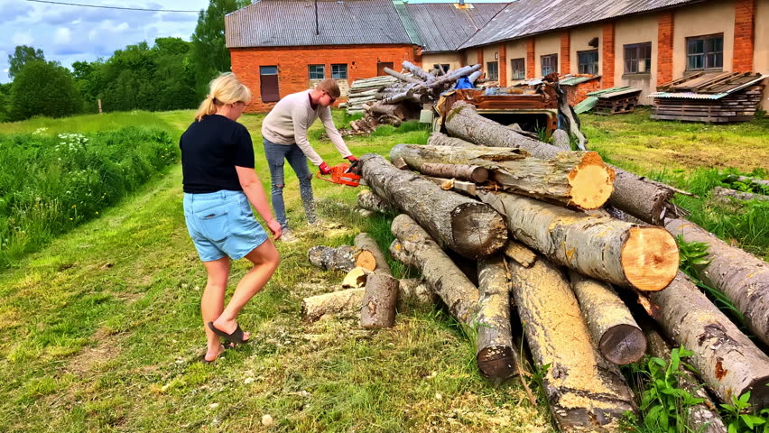 Woman carrying wood as man uses chainsaw to cut logs near countryside farmhouse - Powered by Shutterstock - Get 15% off with code: PIKWIZARD15
