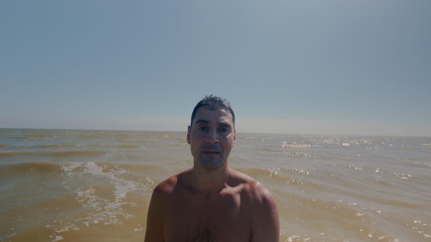 The guy falls backwards into the sea water, standing at a shallow depth. Falling flat into the sea with your back. A man is relaxing by the sea and immersed in salt water.