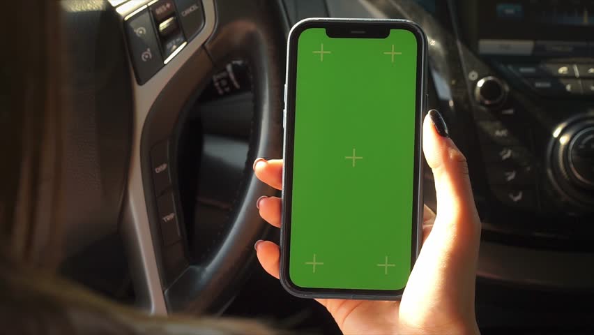 Female hand Holding Mobile Phone with Green Chroma Key Screen Mockup inside Modern Car. Cellphone display close up. Business mockup empty blank space. VFX Motion Tracking Markers.