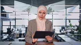 Focused young arabian entrepreneur businesswoman holding digital pc tablet sitting at desk in modern office. Smiling middle eastern woman in suit and hijab working using touchpad computer. Copy space - Powered by Shutterstock - Get 15% off with code: PIKWIZARD15