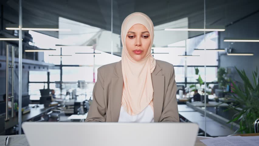 Focused Indian or arabian businesswoman working in office. Copy space. Middle eastern muslim woman in hijab using laptop computer for business analysing, trading, banking, financial data or insurance