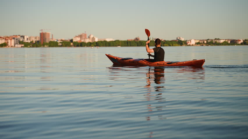 Kayaker paddling on calm lake with city skyline