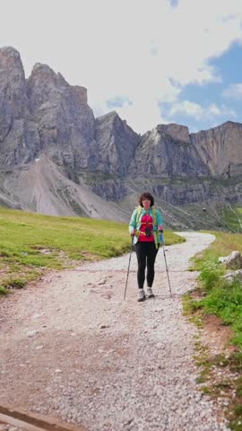 Woman hiking along winding trail in alpine landscape with rocky Dolomites peaks in the background, Italy