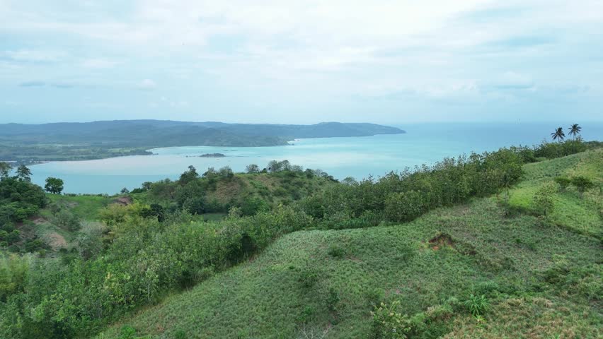 Coastal landscape with turquoise ocean, green hills, and cloudy atmosphere, ideal for nature backgrounds, travel inspiration, and summer holidays.