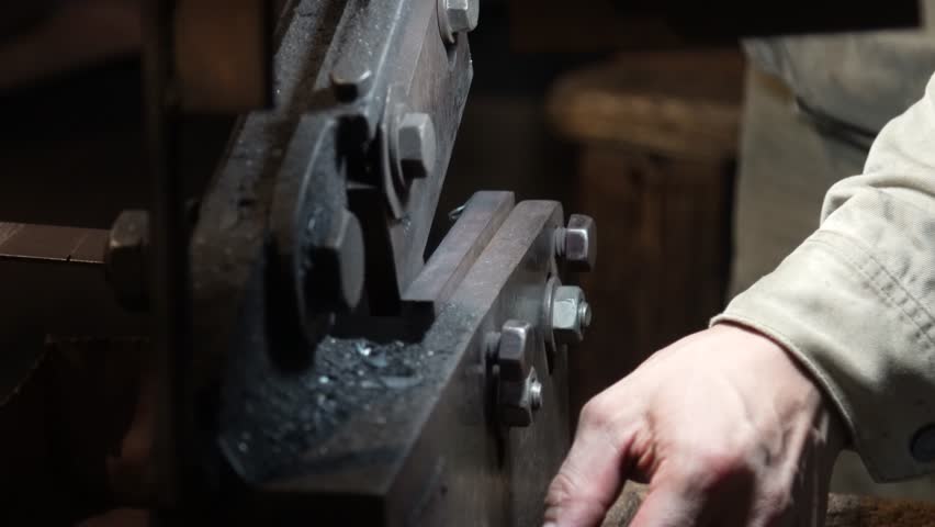 A craftsman uses a hand shear to cut the material into the shape of a knife