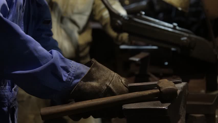 A craftsman uses a hand shear to cut the material into the shape of a knife